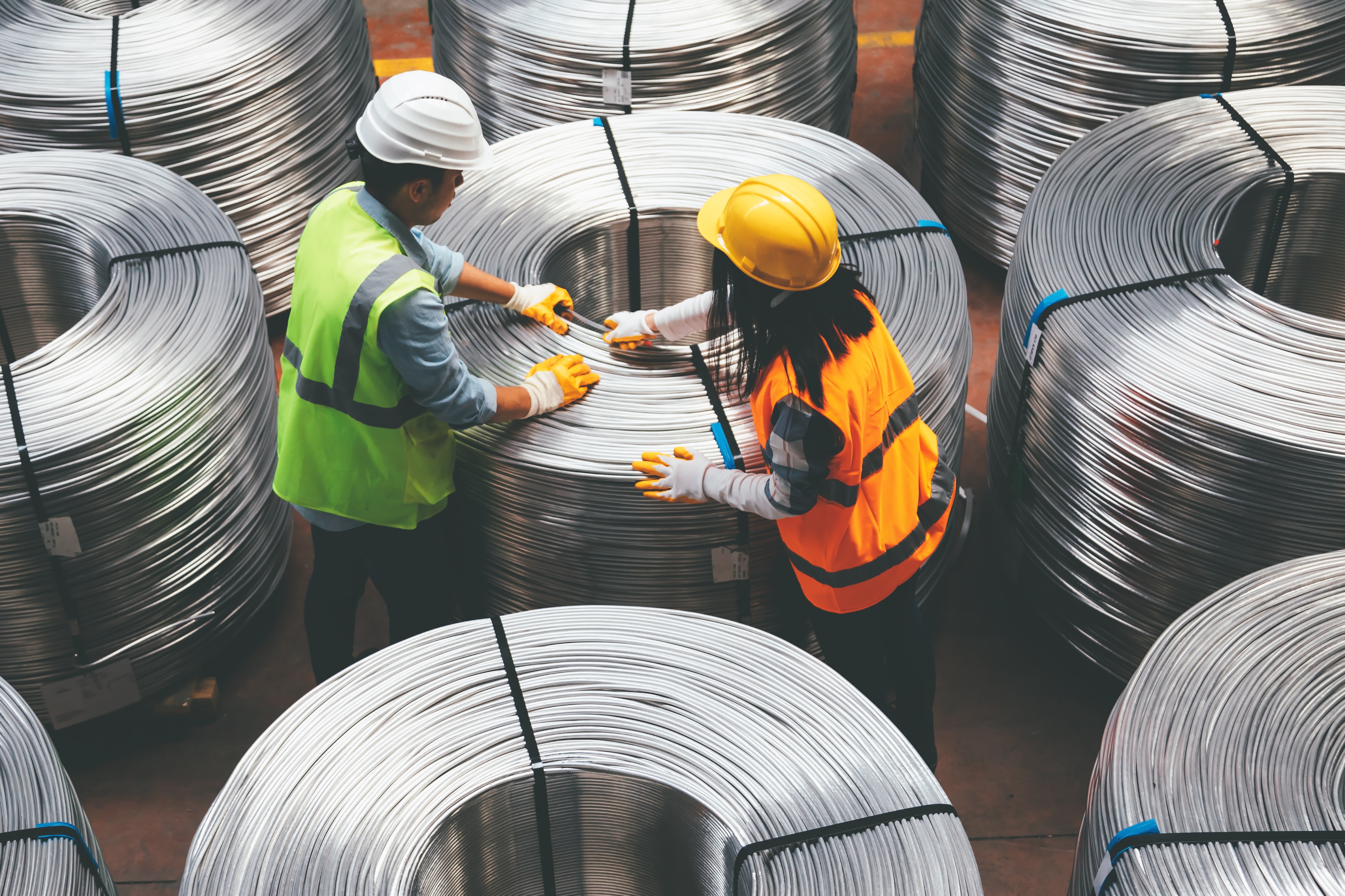 Aerial view of young engineer man and industrial worker woman checking production line and testing quality of steel pipe coils at warehouse section in cable factory. XXXL Iron ore and steelmaking