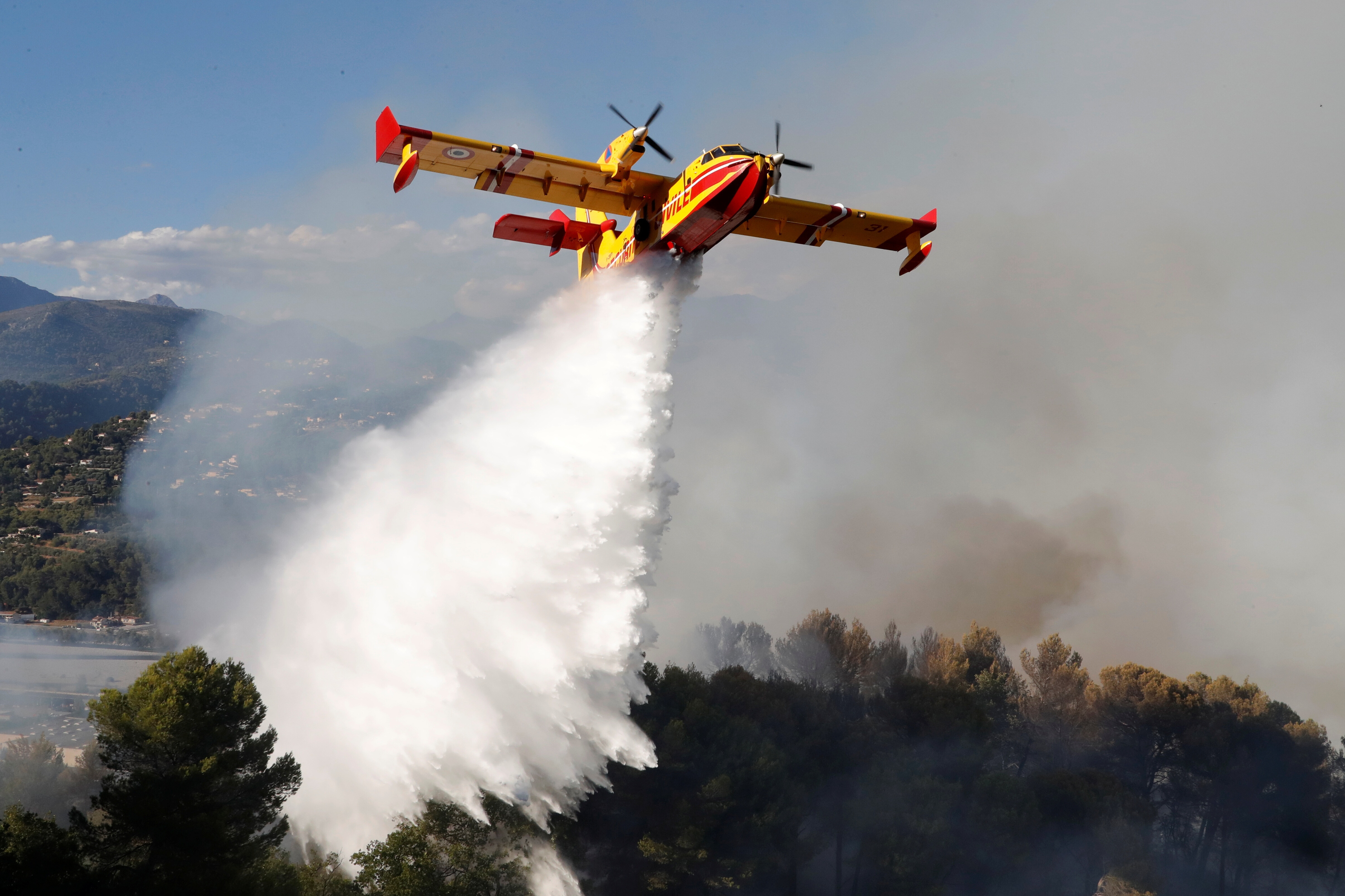 A Canadair firefighting aircraft drops water on a wildfire which burns a forest in Carros, near Nice, France, July 24, 2017.