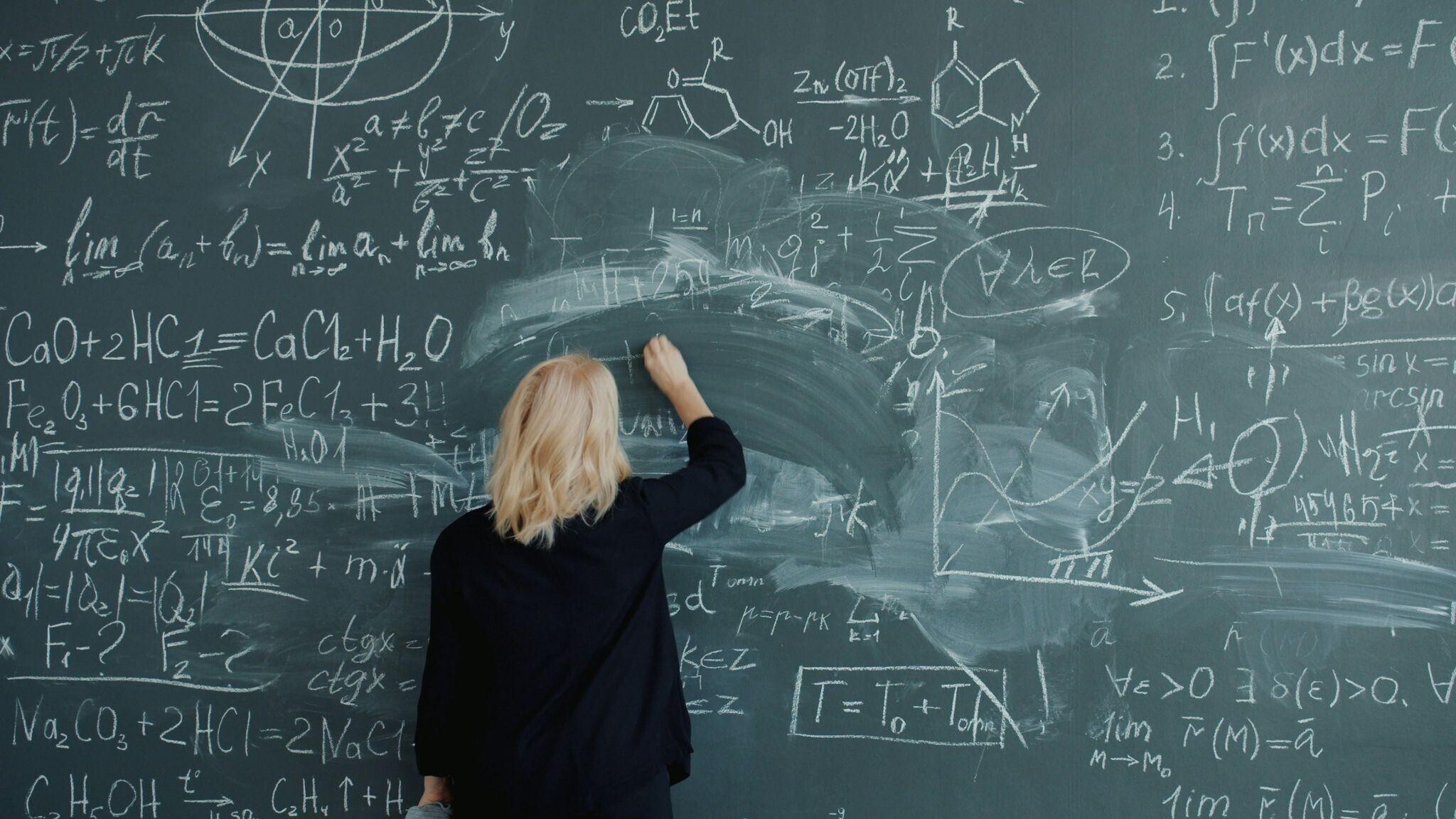 A woman writes equations on a blackboard.