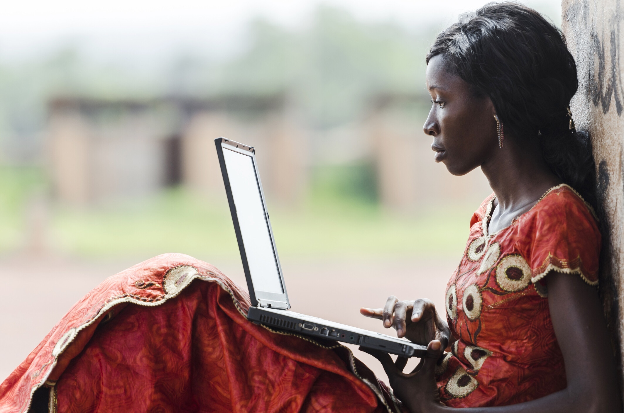 Informal economy: Street Shot of an African Ethnicity young woman working on business holding her technology item computer in a university in Bamako, Mali. Blurred background. University high school environment.