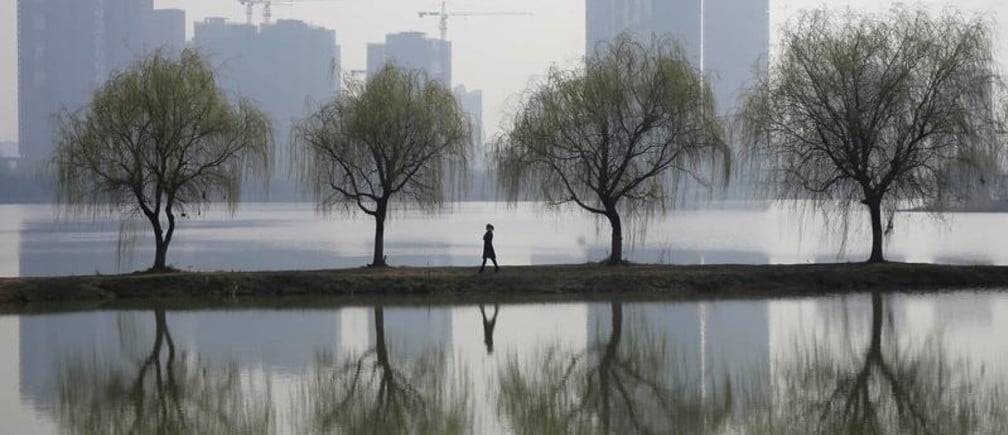 A woman walks past trees reflected on a lake in front of a construction site of a residential compound on a hazy day in Wuhan, Hubei province March 6, 2015. China aims to grow its economy by around 7 percent in 2015 and to keep consumer inflation at around 3 percent, Premier Li Keqiang said in remarks prepared for delivery at today's opening of the annual meeting of parliament, the National People's Congress. REUTERS/Stringer (CHINA - Tags: ENVIRONMENT BUSINESS CONSTRUCTION REAL ESTATE TPX IMAGES OF THE DAY) CHINA OUT. NO COMMERCIAL OR EDITORIAL SALES IN CHINA - GM1EB36182X01