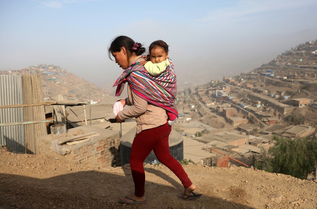 A woman carrying a baby walks on the hills of Villa Maria del Triunfo, a shanty town on the outskirts of Lima, Peru May 9, 2017. Picture taken May 9, 2017. REUTERS/Guadalupe Pardo - RTS161SL