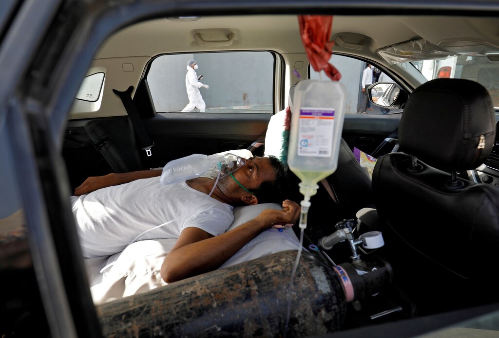 A patient with breathing problems lies inside a car while waiting to enter a COVID-19 hospital for treatment