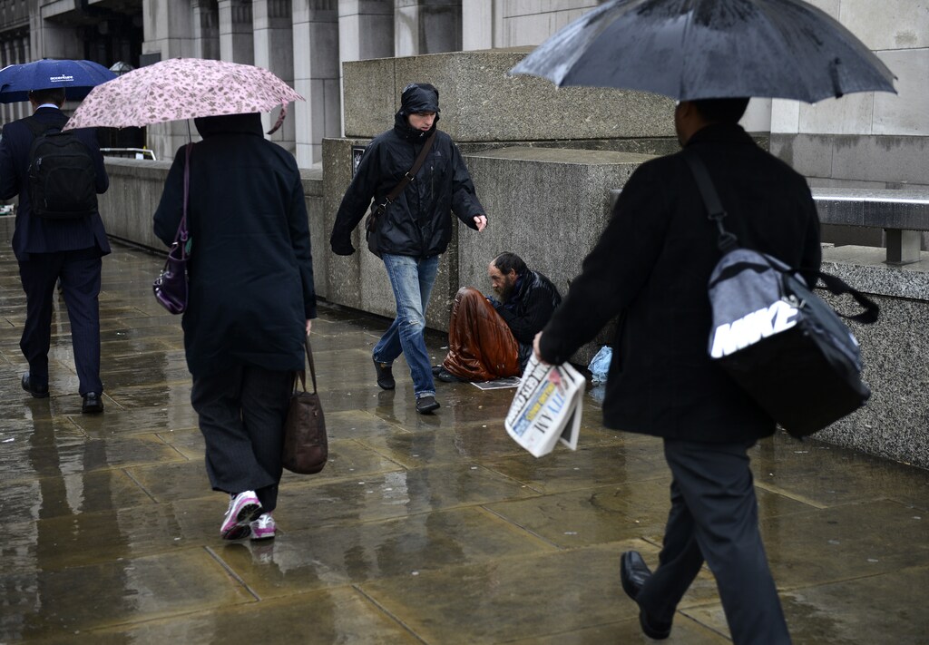 A homeless man sits in the rain as commuters make their way to work across London Bridge