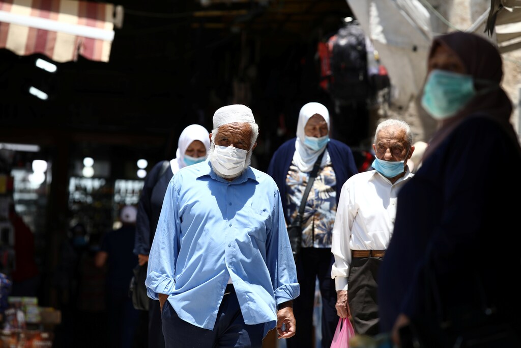 People wearing face masks to help fight the spread of the coronavirus disease (COVID-19) walk past shops in a market in Jerusalem's Old City July 6, 2020. REUTERS/Ammar Awad - RC2NNH99644G