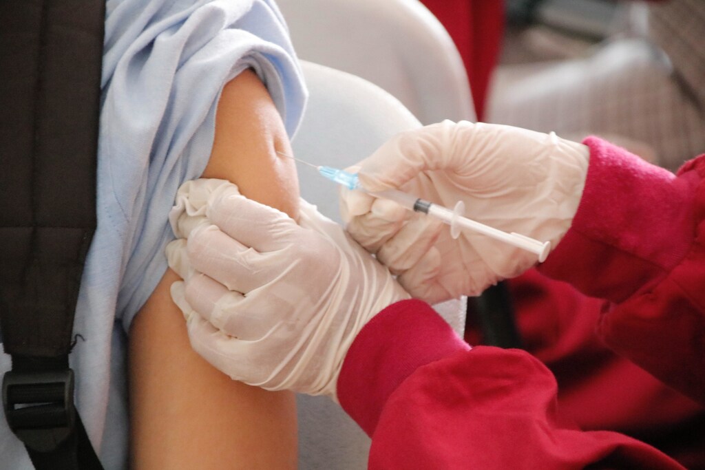 A person wearing gloves injecting a vaccine into an arm using a needle.