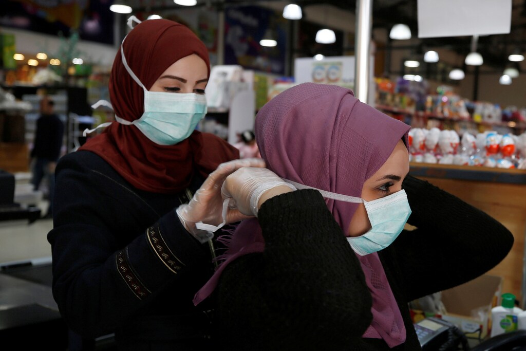 A Palestinian cashier is helped by her colleague to wear a mask amid coronavirus precautions, in a supermarket in Gaza City March 8, 2020. Picture taken March 8, 2020. REUTERS/Mohammed Salem - RC2EGF9WAML5