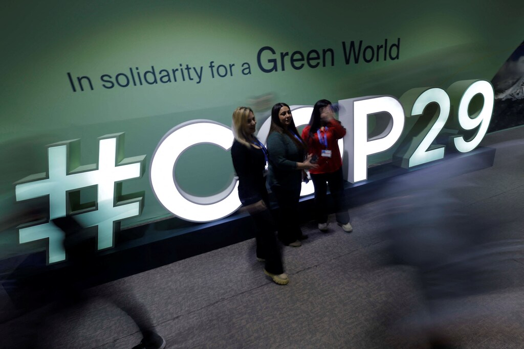 Women pose for a picture as people pass by the logo of the United Nations Climate Change Conference (COP29), in Baku, Azerbaijan November 15, 2024. REUTERS/Maxim Shemetov