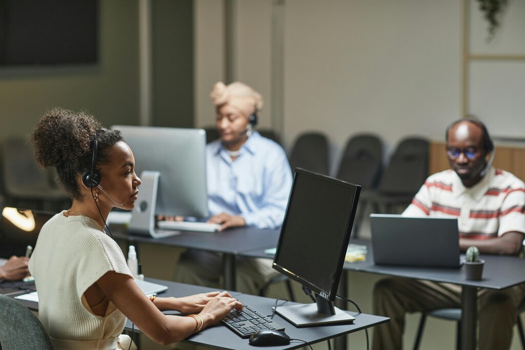 A woman on a computer with headset and two other people on computers with headsets in the background: Making AI Work For Government: A Readiness Framework is a new report that demystifies agentic AI
