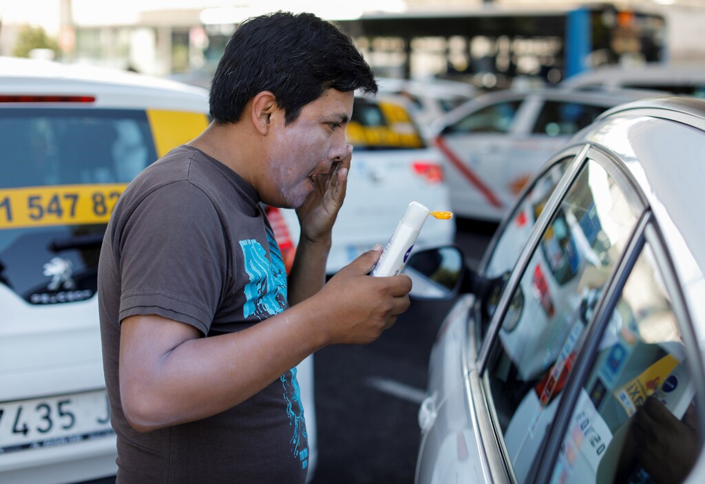A taxi driver puts on sunscreen as taxis block a section of the main avenue Paseo de la Castellana during an indefinite strike against what they say is unfair competition from ride-hailing and car-sharing services such as Uber and Cabify in Madrid, Spain, July 31, 2018. REUTERS/Paul Hanna - RC1C56294B40