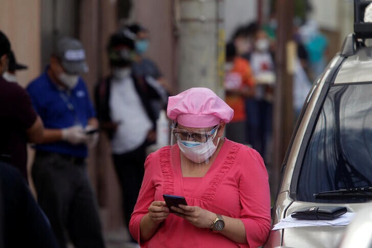 A woman checks her phone while waiting in line to be tested for the coronavirus disease (COVID-19), outside a private lab in Tegucigalpa, Honduras June 12, 2020. REUTERS/Jorge Cabrera