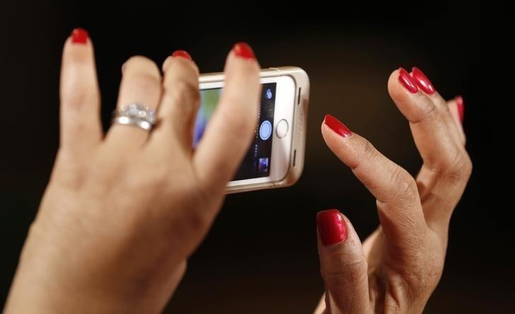 A woman takes a photo as U.S. President Barack Obama holds an event aimed at increasing transparency about women's pay during an event at the White House in Washington April 8, 2014. Obama signed two executive actions, part of a continuing effort by the administration to ensure women are paid equally to their male counterparts for similar work. REUTERS/Kevin Lamarque (UNITED STATES - Tags: POLITICS BUSINESS EMPLOYMENT)