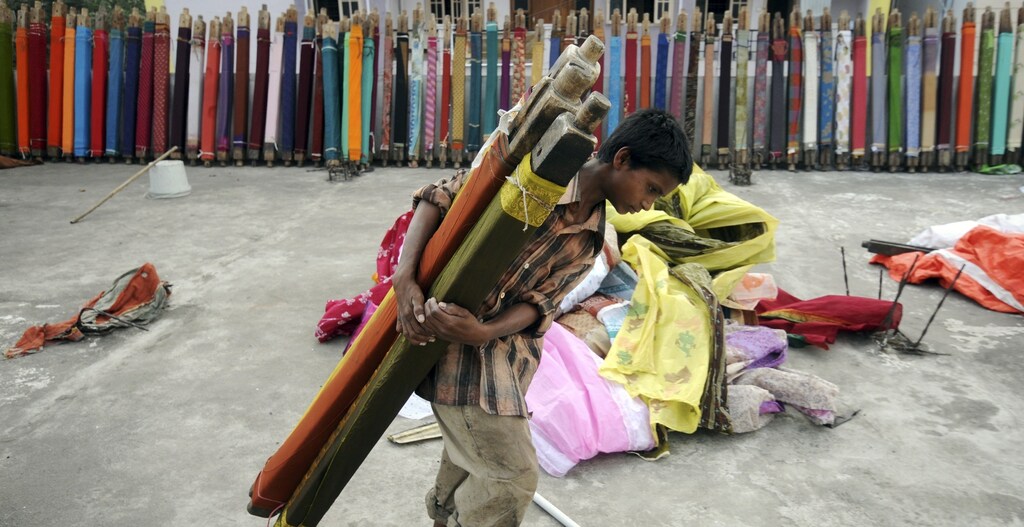 Mohammed Zakir, (13), carries rolls of sarees, a traditional cloth used for women's clothing, for drying after washing them on the terrace of a building in the southern Indian city of Hyderabad June 30, 2011.