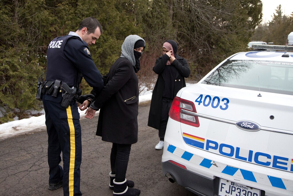 Two women claiming to be from Yemen are detained by a Royal Canadian Mounted Police (RCMP) officer after crossing the U.S.-Canada border into Hemmingford, Quebec, Canada February 22, 2017. REUTERS/Christinne Muschi - RTSZVYO