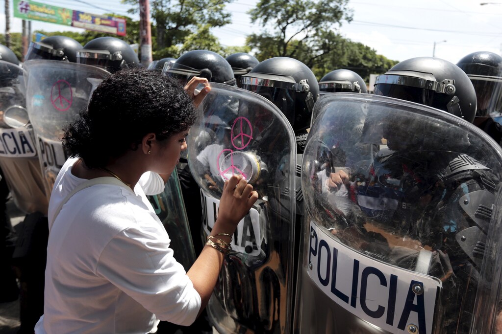 An opposition supporter draws peace signs on the shield of a riot police officer during a protest in front of the Supreme Electoral Council (CSE) building in Managua, Nicaragua August 5, 2015. The protesters said they were demonstrating to demand fairer elections in the country next year. REUTERS/Oswaldo Rivas - GF20000014620