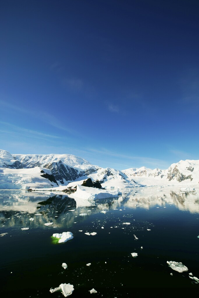 Bright sunny day in Antarctica. Full calm and reflection of icebergs in deep clear water. Travel by the ship among ices. Snow and ices of the Antarctic islands: Black carbon, a significant contributor to Arctic warming, accelerates ice and snow melting.