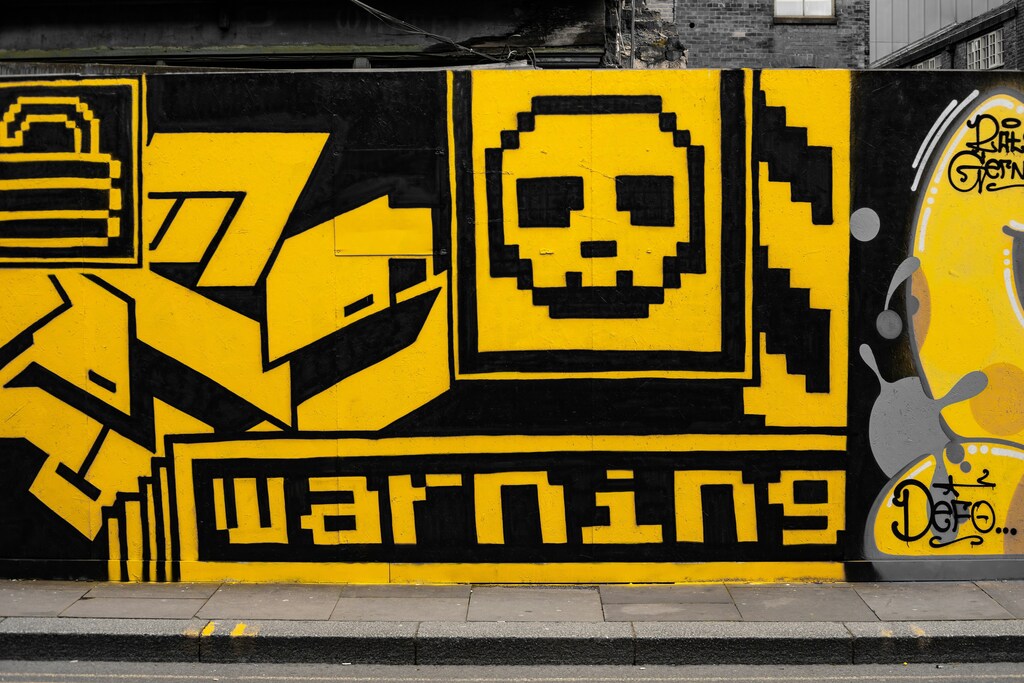 Black and yellow street art depicting a graphic skull and cross bones above the word warning: cybercrime