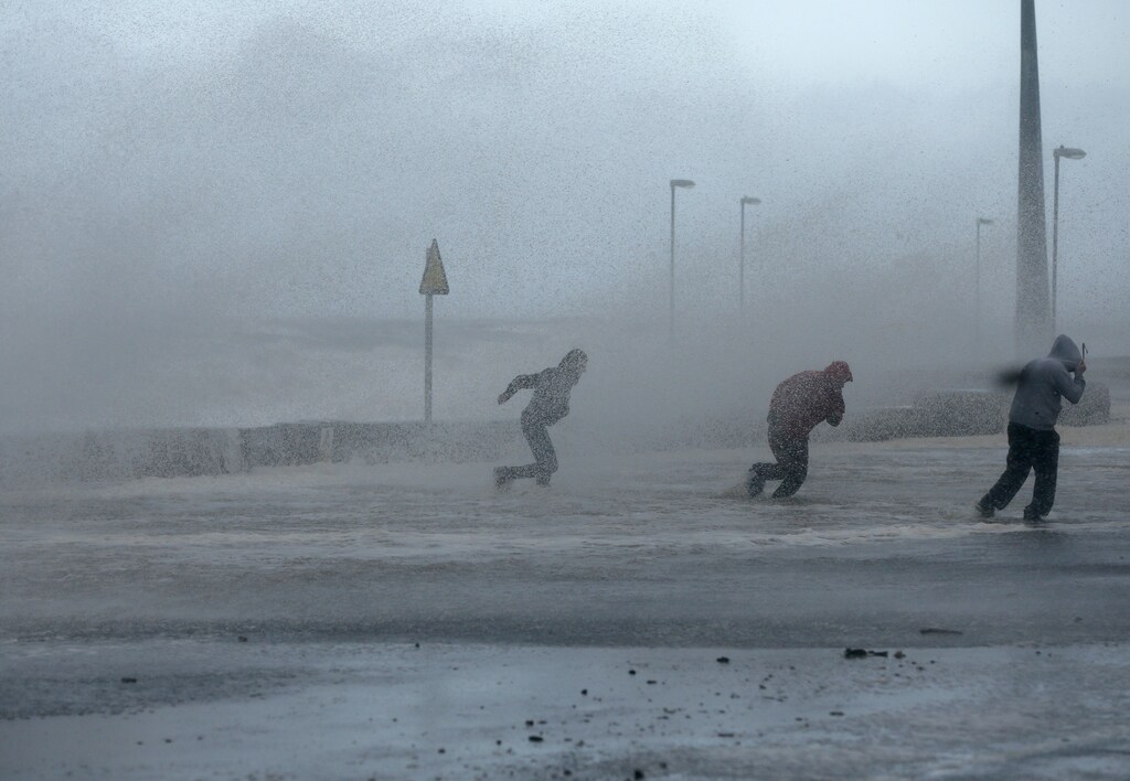 People run through sea spray in Rhyl, north Wales December 5, 2013. Hurricane-force winds disrupted transport and power supplies in Scotland and threatened costal flooding in England as they closed on northern Europe in what meteorologists said could be one of the most powerful storms to hit the continent in years. REUTERS/Phil Noble (BRITAIN - Tags: DISASTER SOCIETY) - LR1E9C513NOAK