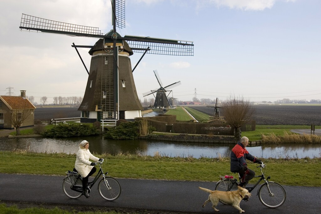 Two Dutch bicyclists pass one of four windmills of the Viermolengang, built in 1785, in Zevenhuizen, the Netherlands, February 7, 2007. To raise money and draw tourists, the Dutch Windmill Association has proclaimed 2007 "The Year of the Windmill" in the hopes of attracting tourists and investment. Photo taken February 7, 2007. REUTERS/Michael Kooren (NETHERLANDS) - GM1DUPIWQEAA