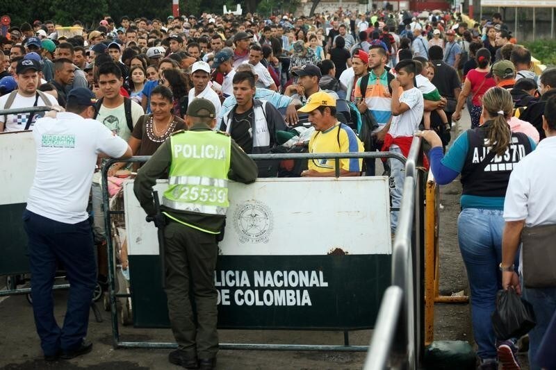 A Colombian police officer and a migration officer stand in front of people who are attempting to cross into Colombia from Venezuela through Simon Bolivar international bridge, at Cucuta, Colombia, July 25, 2017. REUTERS/Luis Parada - RC191984B120