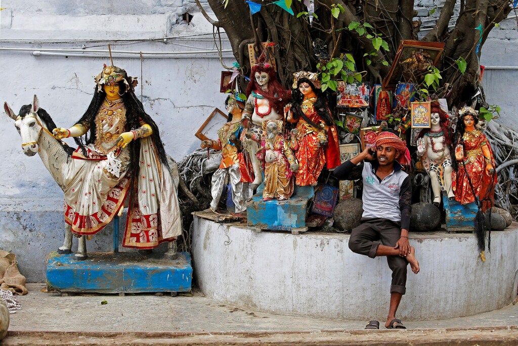 A labourer speaks on his mobile phone as he takes rest in front of idols of Hindu deities which are kept under a tree at a market area in Kolkata, India, April 2, 2018. REUTERS/Rupak De Chowdhuri TPX IMAGES OF THE DAY - RC1570C0DAF0