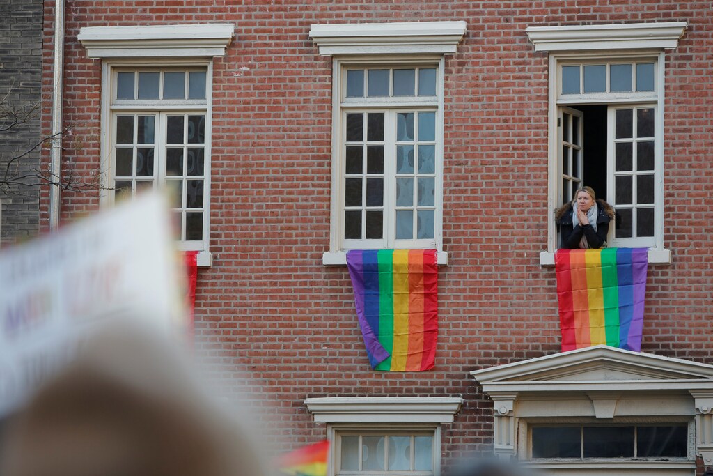 A woman looks on from a nearby window over a gathering of the LGBTQ community and supporters protesting U.S. President Donald Trump's agenda in Manhattan, New York, U.S., February 4, 2017. REUTERS/Andrew Kelly - RTX2ZNJQ