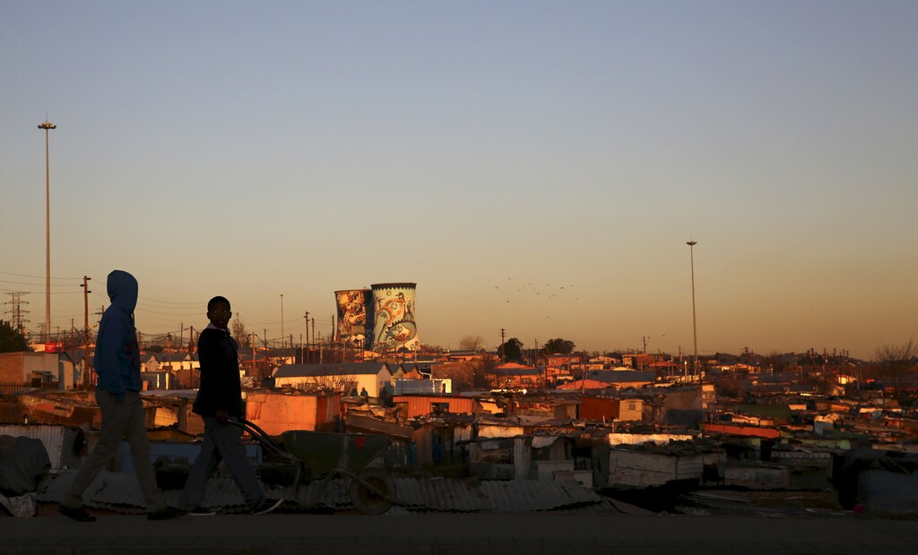 Unused cooling towers are seen overlooking an informal settlement as locals walk before sunset in Soweto, South Africa August 5, 2015. REUTERS/Siphiwe Sibeko - RTX1N78T