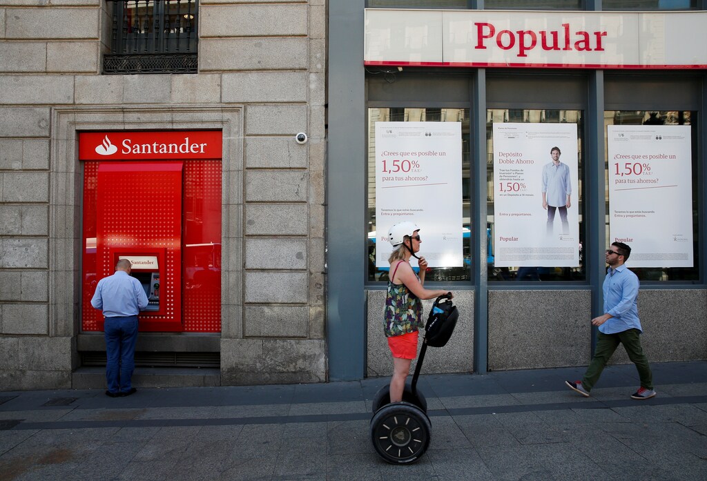A man uses a cash dispenser at a branch of Spain's biggest bank Santander next to a Banco Popular branch on the same day Santander announced that it would buy struggling rival Banco Popular for a nominal one euro after European authorities determined the lender was on the verge of insolvency, in Madrid, Spain June 7, 2017. REUTERS/Juan Medina TPX IMAGES OF THE DAY - RTX39FTA
