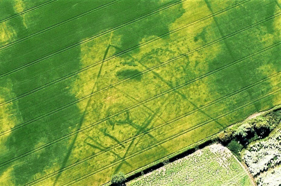 Unseen from ground level, this Iron Age farmstead with recognisable round house near the Yorkshire Wolds is revealed in cropmarks. The lighter green shows it was carefully placed on a gravel rise surrounded by wetter land, shown here where the crop grows a darker green.