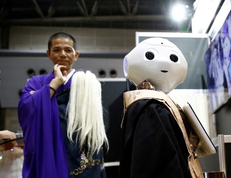 A Buddhist monk looks at a 'robot priest' wearing a Buddhist robe during its demonstration at Life Ending Industry EXPO 2017 in Tokyo, Japan August 23, 2017.