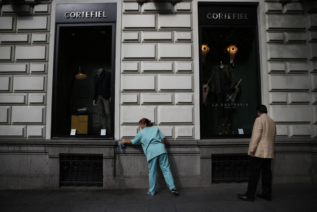 A man window shops as a woman cleans the outside of a clothing store in Madrid September 26, 2014. Spain's government on Friday raised the economic growth outlook for 2014 and 2015, revising the former to 1.3 percent from a previous forecast of 1.2 percent, slightly less than expected. REUTERS/Susana Vera (SPAIN - Tags: BUSINESS SOCIETY) - RTR47UAS