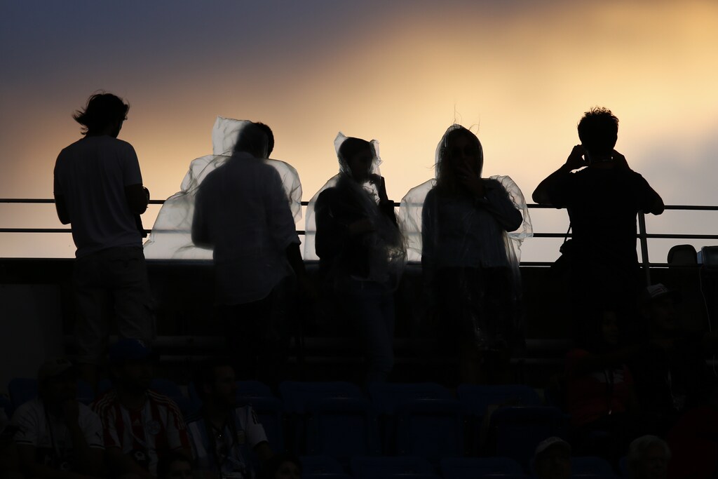 Fans wearing rain ponchos are backlit as they watch the sunset from Arthur Ashe Stadium ahead of the mens final between Roger Federer of Switzerland and Novak Djokovic of Serbia at the U.S. Open Championships tennis tournament in New York, September 13, 2015. REUTERS/Carlo Allegri - TB3EB9E00WFLJ