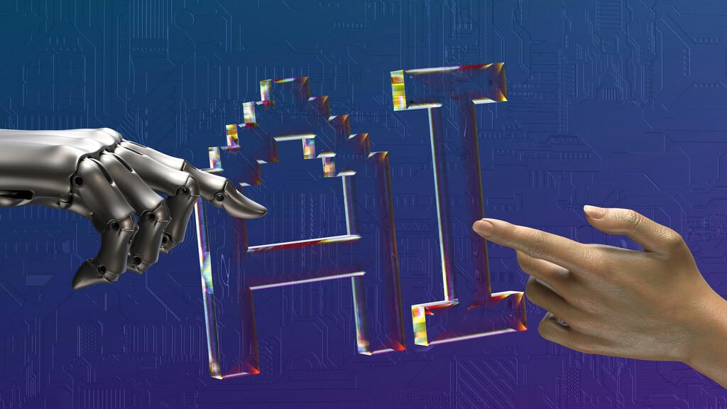 A robot hand and a human hand point towards computer-generated text that reads "AI".