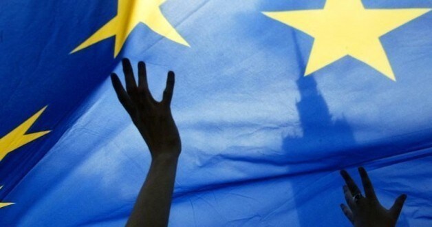 People wave an European Union flag in front of the Palace of Culture during a EU parade in Warsaw May 15, 2005. A few hundred people marched through the Polish capital to celebrate European unity and express support for Ukraine's' EU ambitions before the Counc