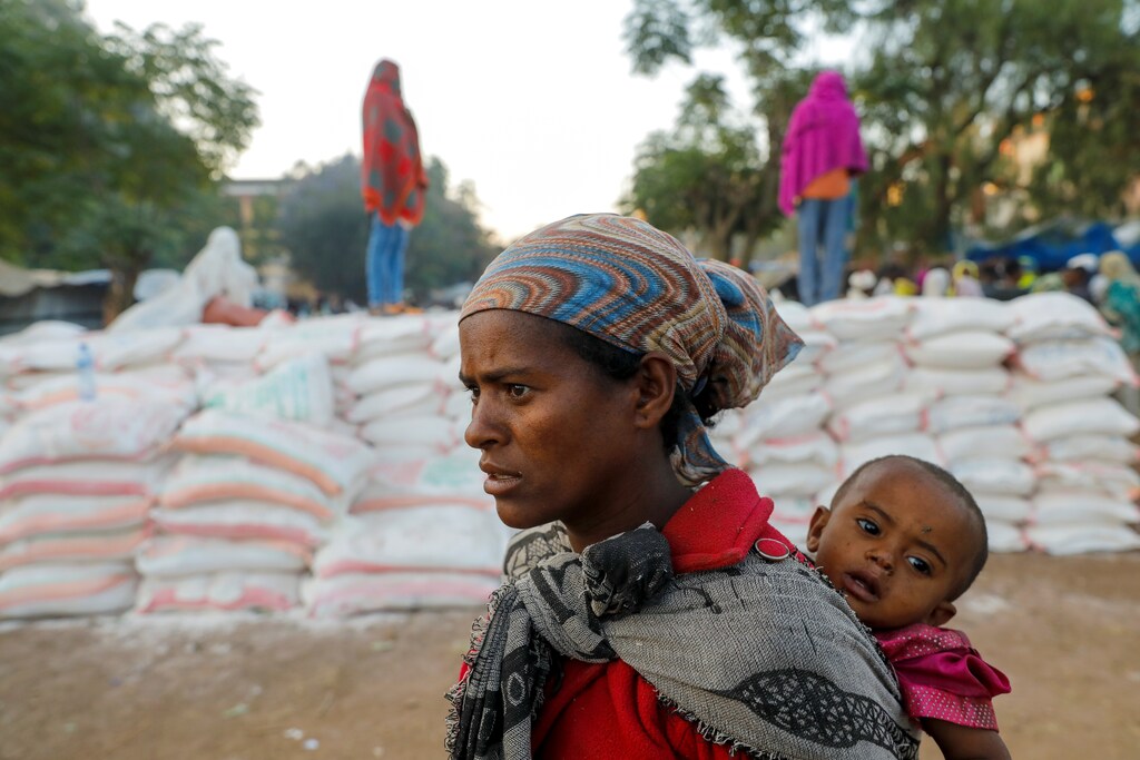 A woman carries an infant as she queues in line for food, at the Tsehaye primary school, which was turned into a temporary shelter for people displaced by conflict, in the town of Shire, Tigray region, Ethiopia, March 15, 2021. Picture taken March 15, 2021.