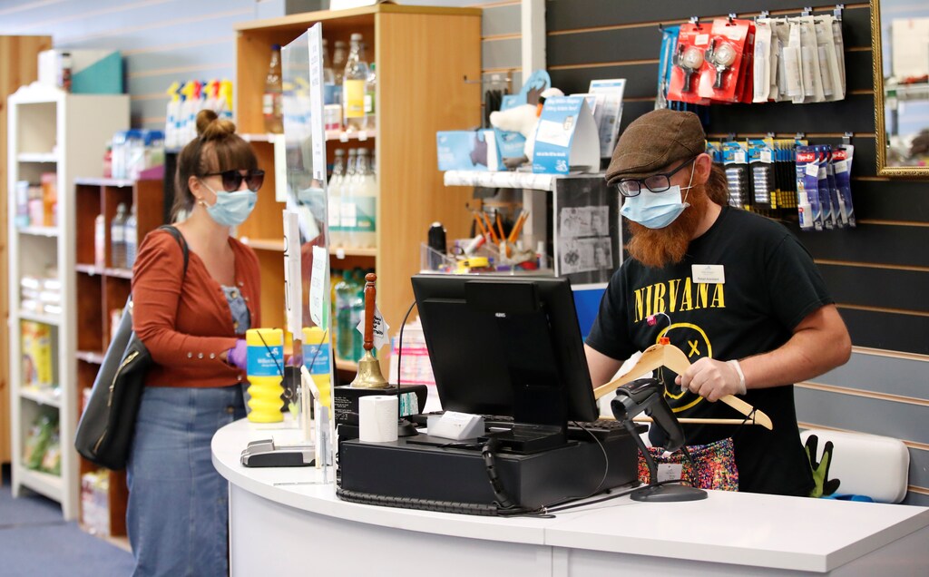 A woman wearing a face mask, buys a second-hand garment at a charity shop in London, United Kingdom.