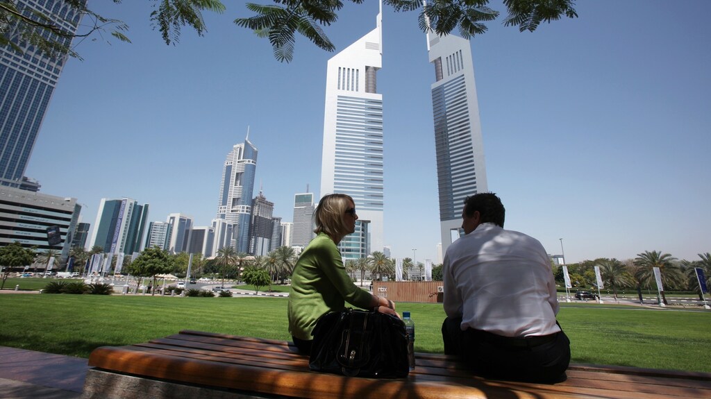 People sit on a bench in front of the Emirates Towers at the Dubai International Financial Centre March 21, 2010.