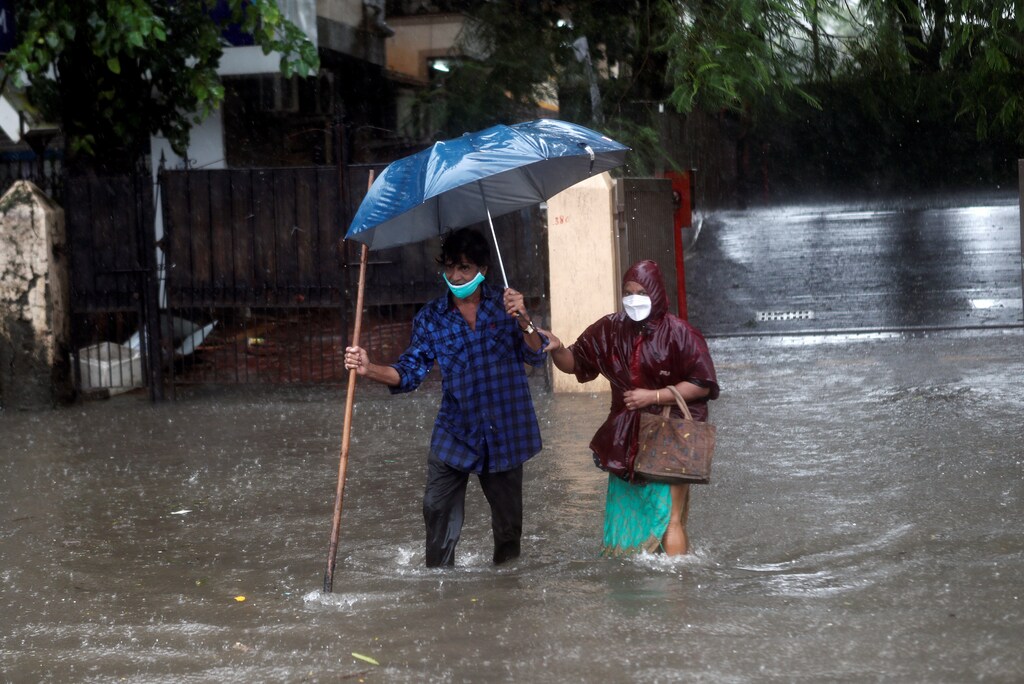 A man helps a woman cross a waterlogged road after heavy rainfall in Mumbai, India, August 5, 2020.