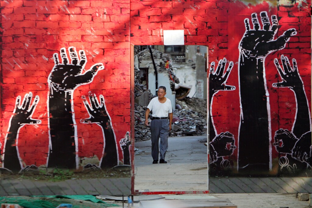 A man walks towards a fence that is painted with an advertisement in Shanghai August 2, 2006. The fence covers a district undergoing demolition. REUTERS/Aly Song (CHINA) - GM1DTELHMRAA