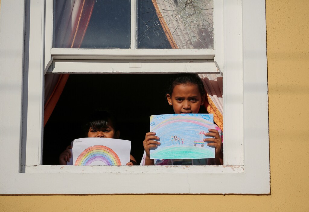 Bashierah Moos, 5, and Hanaa Moos, 9, pose for a photograph while holding pictures that they drew during the coronavirus disease (COVID-19) outbreak, as they stand by a window at their house in Cape Town, South Africa, April 19, 2020. Bashierah drew a picture of a rainbow and Hanaa said "I drew my family next to an ice-cream truck because I miss, I miss going out." She added "I feel sad because I can't see my friends and go to school." REUTERS/Sumaya Hisham SEARCH "CORONAVIRUS DRAWING" FOR THIS STORY. SEARCH "WIDER IMAGE" FOR ALL STORIES. - RC2BAG92O3MV