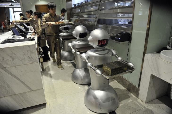 A man puts dishes on robots for delivery at a restaurant in Hefei, Anhui province, December 26, 2014. The restaurant, with a space of 1300 square metres and a total of 30 robots to cook meals, deliver dishes and welcome costumers, was reported to be the biggest robot restaurant in China. REUTERS/STRINGER (CHINA - Tags: SOCIETY BUSINESS FOOD SCIENCE TECHNOLOGY) CHINA OUT. NO COMMERCIAL OR EDITORIAL SALES IN CHINA