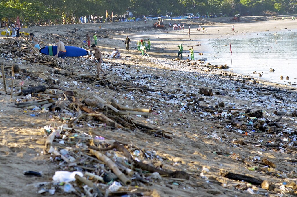 Tourists walk amongst trash washed up on Kuta beach by seasonal winds, as workers attempt a clean-up in the background, on the Indonesian island of Bali February 15, 2016 in this photo taken by Antara Foto. REUTERS/Wira Suryantala/Antara FotoATTENTION EDITORS - THIS IMAGE HAS BEEN SUPPLIED BY A THIRD PARTY. IT IS DISTRIBUTED, EXACTLY AS RECEIVED BY REUTERS, AS A SERVICE TO CLIENTS. FOR EDITORIAL USE ONLY. NOT FOR SALE FOR MARKETING OR ADVERTISING CAMPAIGNS MANDATORY CREDIT. INDONESIA OUT. NO COMMERCIAL OR EDITORIAL SALES IN INDONESIA. TPX IMAGES OF THE DAY - GF10000309242
