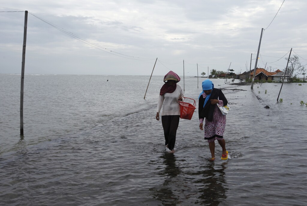 Villagers walk along a street flooded with sea water in Mayangan village in Subang, Indonesia