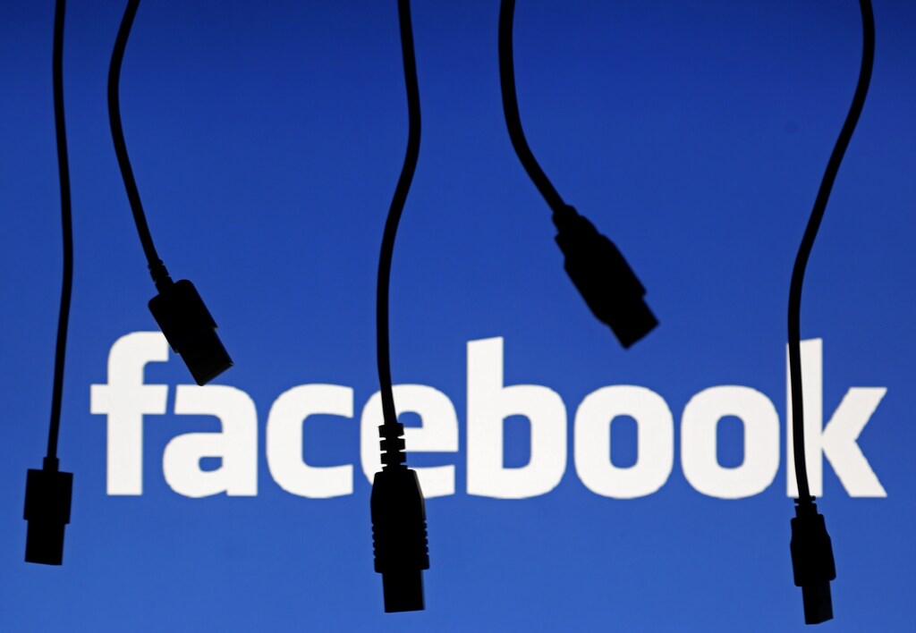 Electronic cables are silhouetted next to the logo of Facebook in this September 23, 2014 illustration photo in Sarajevo. REUTERS/Dado Ruvic (BOSNIA AND HERZEGOVINA - Tags: BUSINESS TELECOMS) - LR1EA9O0V25E7