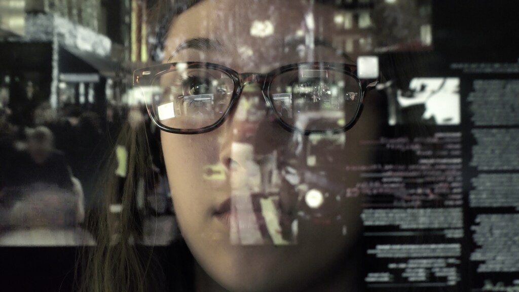 An asian woman concentrating on a touch screen display. The point of view is from behind the screen, looking through the data & images to the woman's face and hands as she manipulates the windows of information. Reading health news