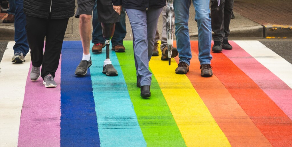 a diverse group of people walk across a pedestrian crossing with rainbow colours to signify the LGBTQ+ movement