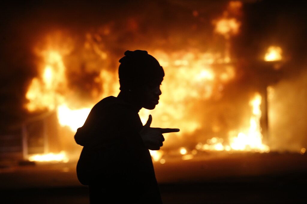 A man walks past a burning building during rioting after a grand jury returned no indictment in the shooting of Michael Brown in Ferguson, Missouri, early November 25, 2014. Gunshots were heard and bottles were thrown as anger rippled through a crowd outside the Ferguson Police Department in suburban St. Louis after authorities on Monday announced that a grand jury voted not to indict a white officer in the August shooting death of an unarmed black teen