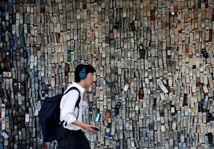 A man using a smartphone walks past an electronic shop's wall decorated with old cell phones which its owner Watanabe Masanao had collected over 20 years is pictured in Tokyo, Japan July 5, 2017. REUTERS/Kim Kyung-Hoon TPX IMAGES OF THE DAY