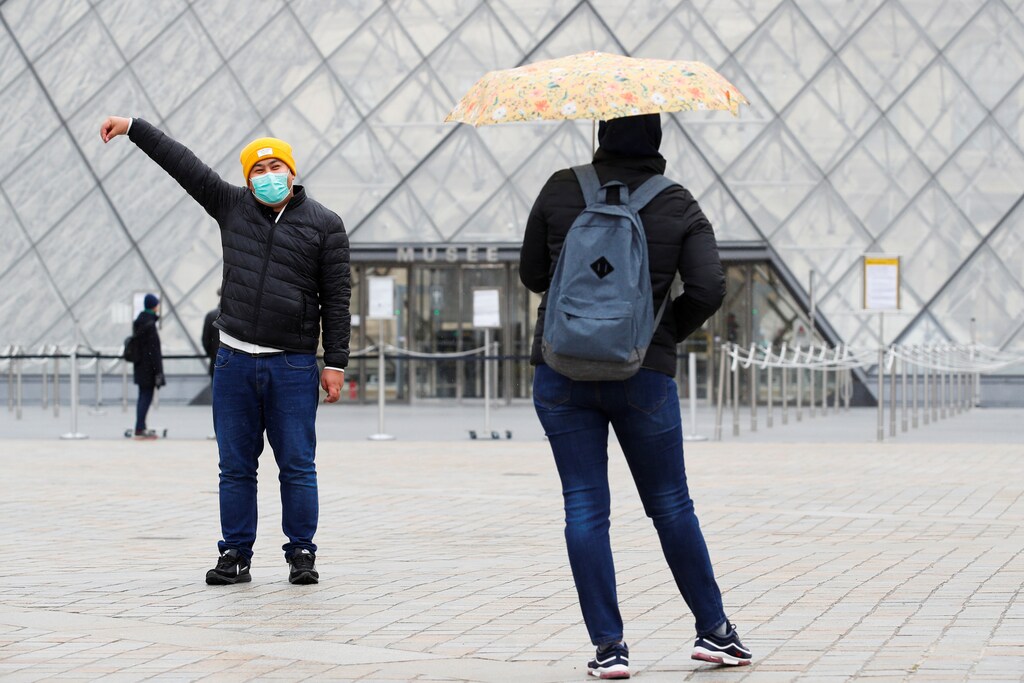 A tourist wearing a protective mask is seen near The Louvre as as the museum among top tourism landmarks closed their doors on Friday after France's government banned gatherings of more than 100 people to curb the spread of coronavirus COVID-19 in Paris, France March 14,2020. REUTERS/Gonzalo Fuentes - RC2QJF9AHKJA