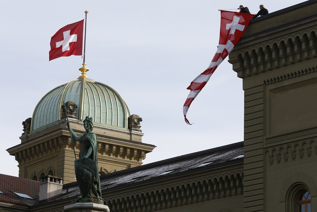 Workers hang up a Swiss flag on the Swiss parliament building in Bern, Switzerland, November 24, 2015. REUTERS/Ruben Sprich - LR1EBBO10FE8G